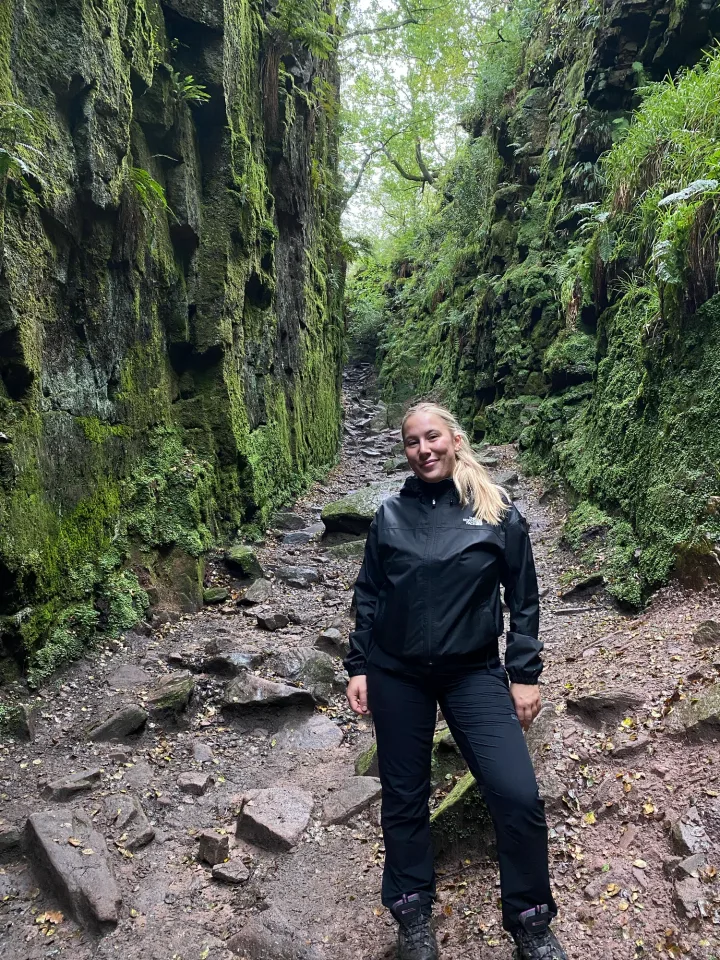 Aimee walking along a wooded path between moss-covered rock walls